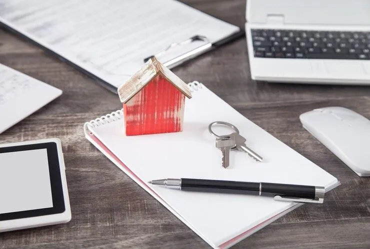 Une maquette de maison en bois posé sur un carnet à côté 'un stylo et des clefs