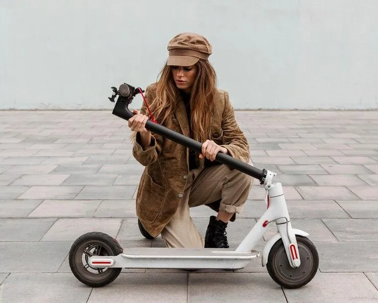 Une femme qui plie sa trottinette électrique dans la rue