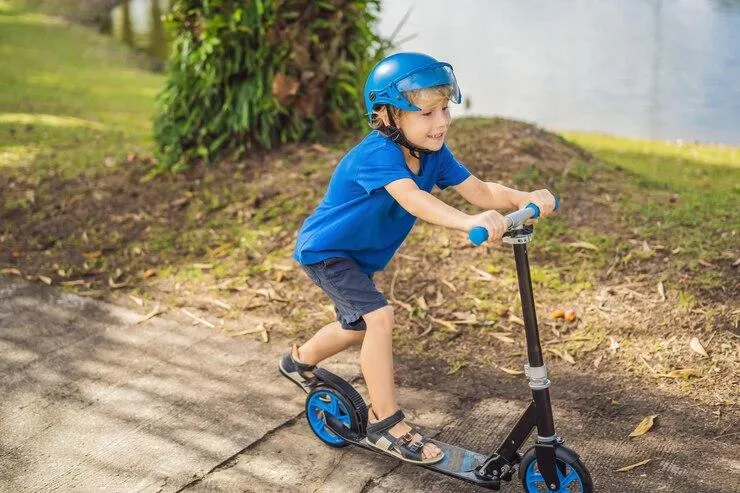 Un petit garçon avec un casque qui joue avec sa trottinette