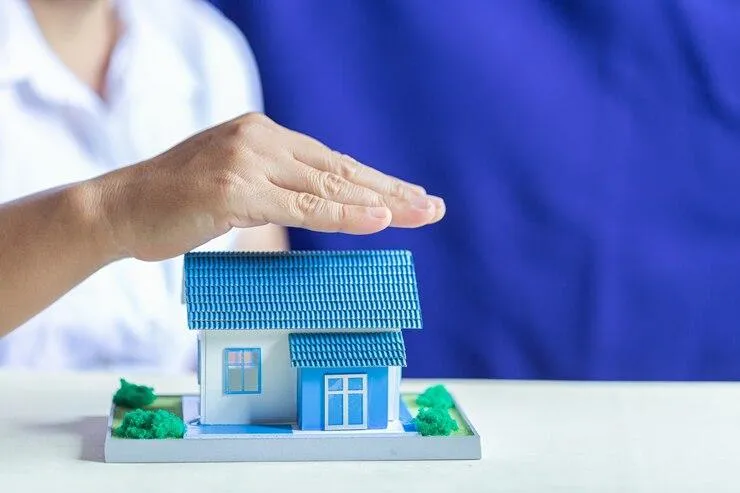 Une maquette de maison bleue recouvert par une main
