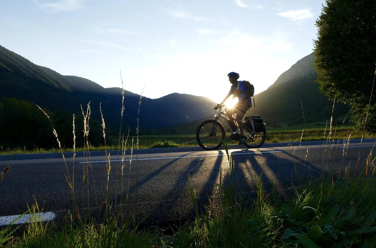 Un homme qui roule à vélo sur une route bordé par des montagnes et de la verdure.