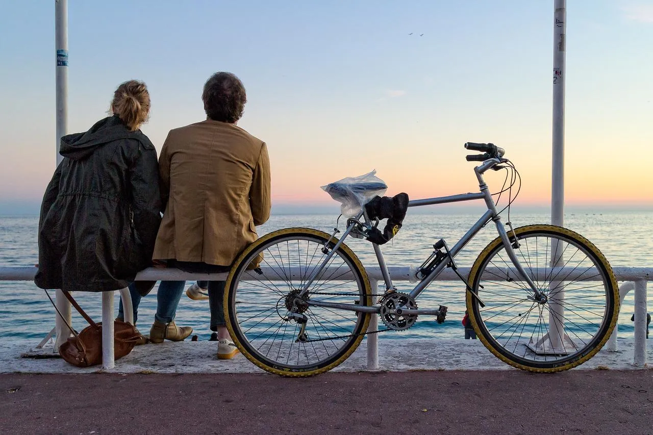 Un couple qui s'assoit au bord de l'eau avec un vélo garé à côté