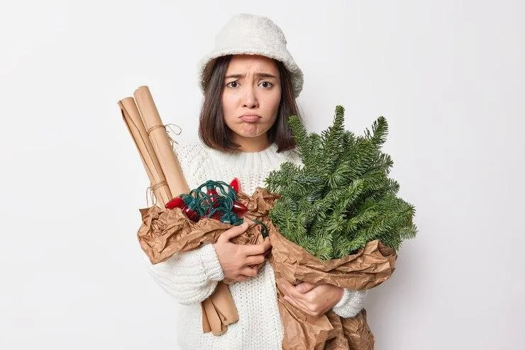 Une femme qui tient des parties de son sapin et ses décorations de Noël en faisant la mou