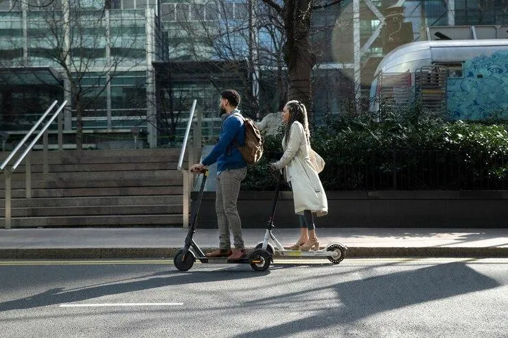 Un homme et une femme roulant chacun sur leur trottinette dans la rue