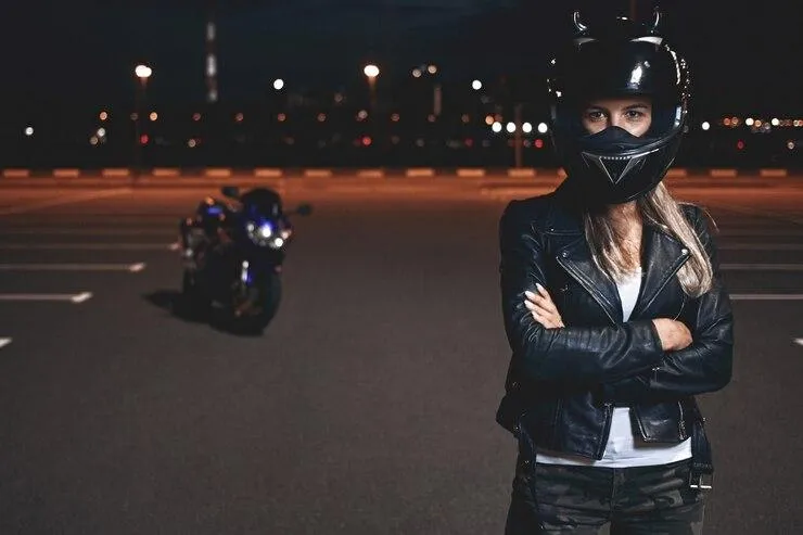 Une femme avec un casque dans un parking de nuit avec une moto à l'arrière