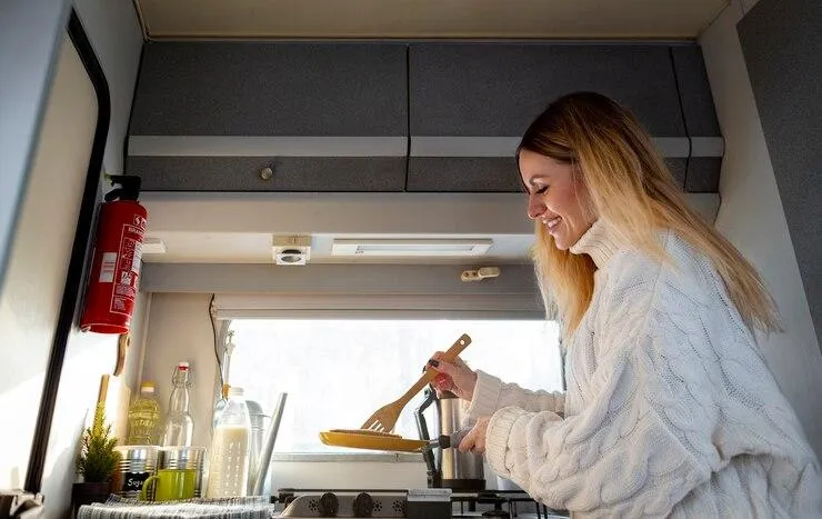 Une femme dans une cuisine qui cuisine à côté d'un extincteur sur le mur