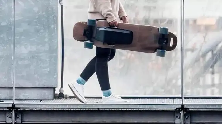 Une personne qui tient un skateboard électrique en marchant