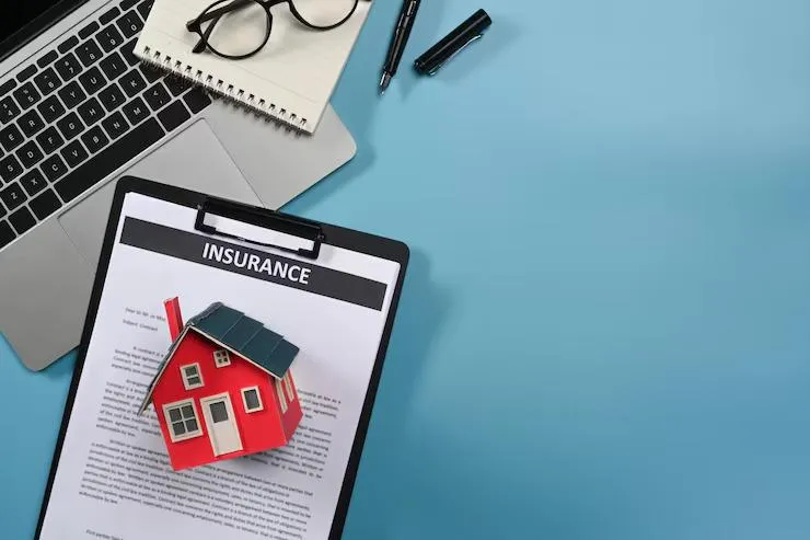 Un document avec marqué INSURANCE placé sous une maquette de maison et près d'un ordinateur portable
