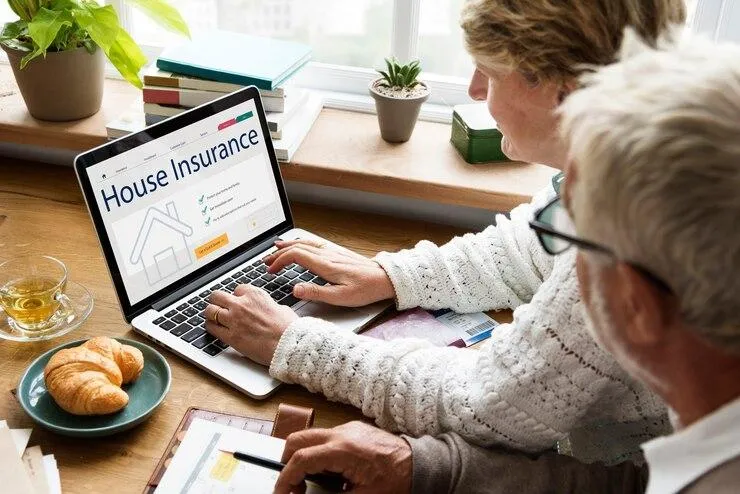 Un couple qui se connecte sur un ordinateur avec HOUSE INSURANCE sur l'écran