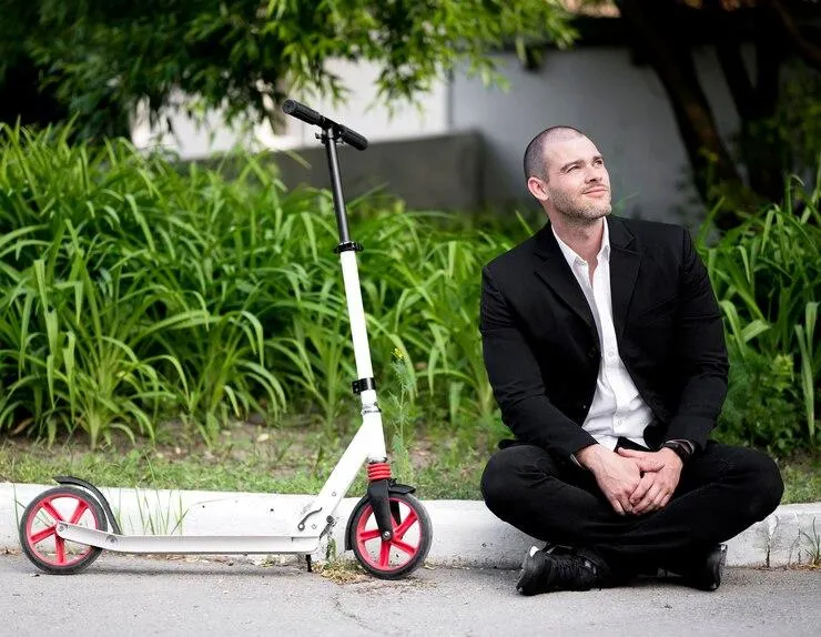 Un homme assis sur le sol à côté d'une trottinette blanche