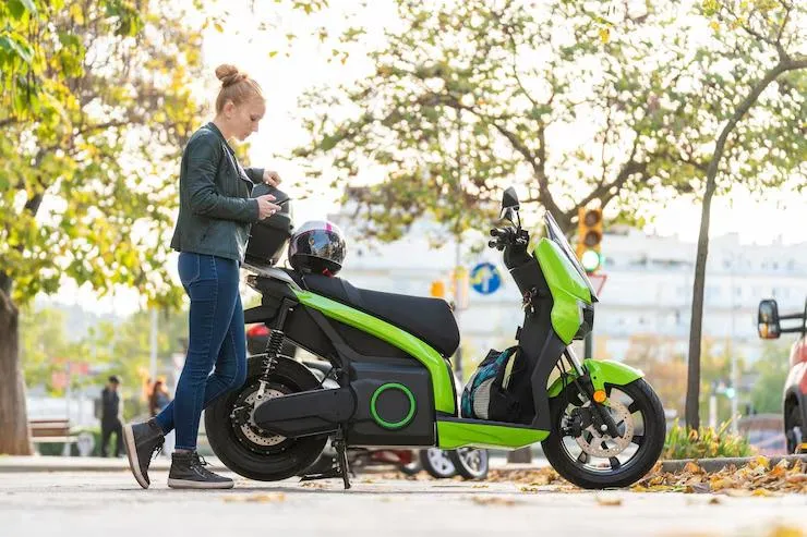 Une femme qui s'avance vers son scooter vert et noir garé dans la rue