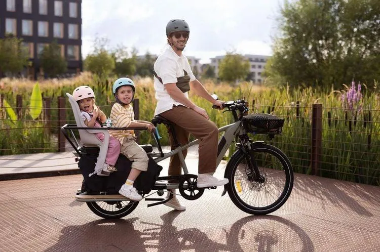 Un homme qui conduit un vélo cargo avec deux enfants à l'arrière