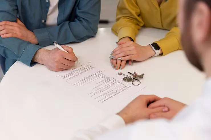 Un homme sur le point de signer un contrat à côté d'une femme et en face d'un homme