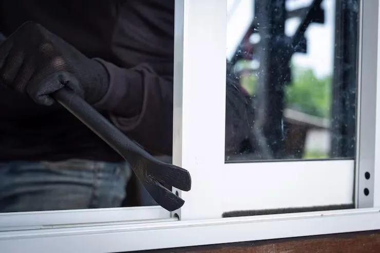 Un homme qui force une fenêtre avec un pied de biche