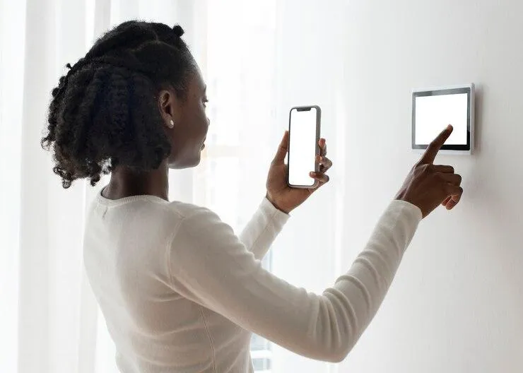 Une femme qui tient son smartphone et qui paramètre une tablette sur un mur