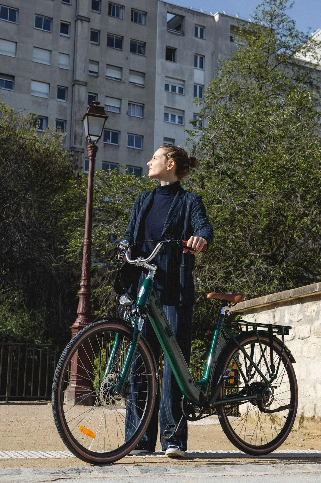 Une femme qui marche avec son vélo dans les mains dans un parc près d'un grand immeuble