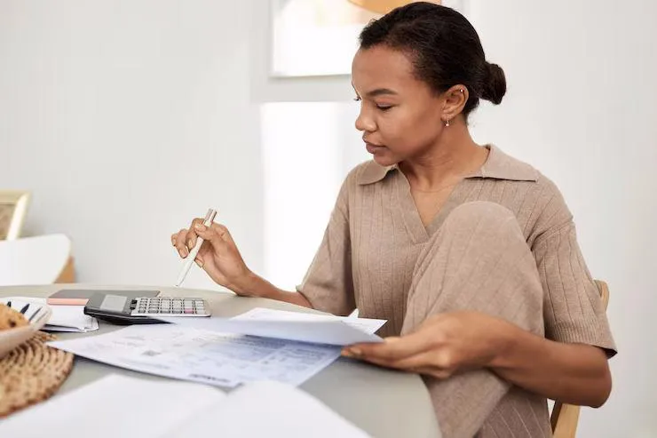 Une femme qui tient des documents en faisant des calculs sur une calculatrice