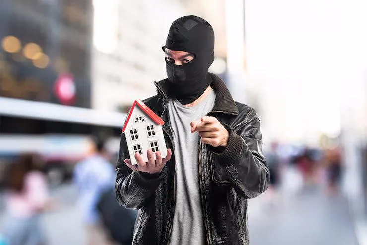 Un homme en masque qui tient une maquette de maison dans sa main
