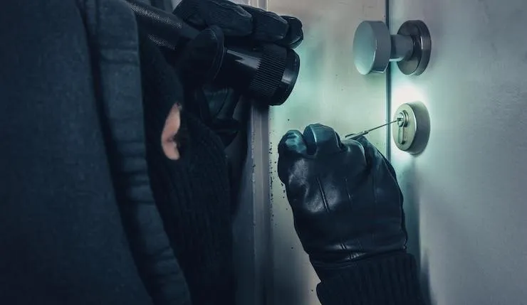 Un homme avec une lampe torche et un kit de crochetage qui tente d'ouvrir une porte