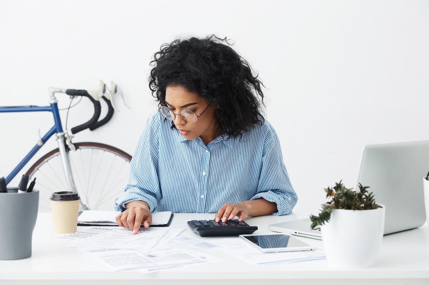 Une femme qui fait des calculs sur une calculatrice en regardant des documents
