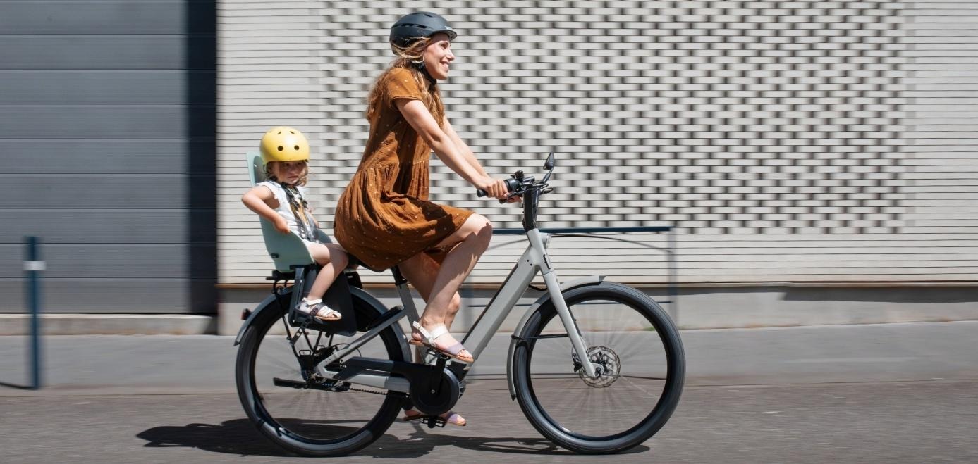 Une femme qui roule en ville avec un enfant sur le vélo électrique urbain Moustache Lundi 27