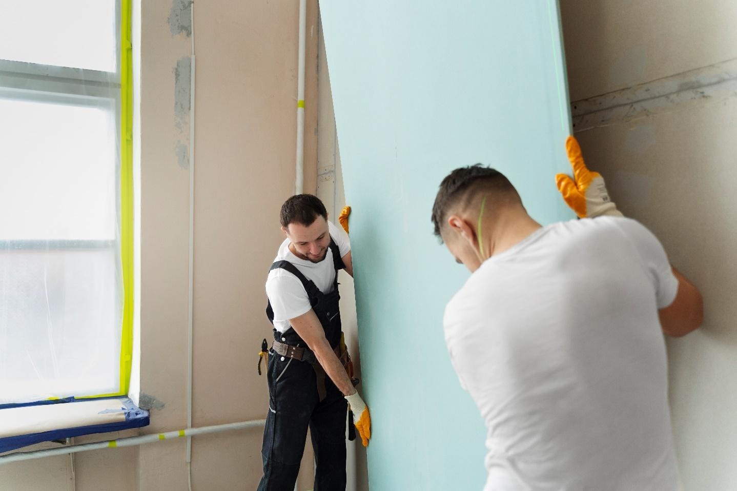 Deux hommes qui installent une plaque de placo contre un mur