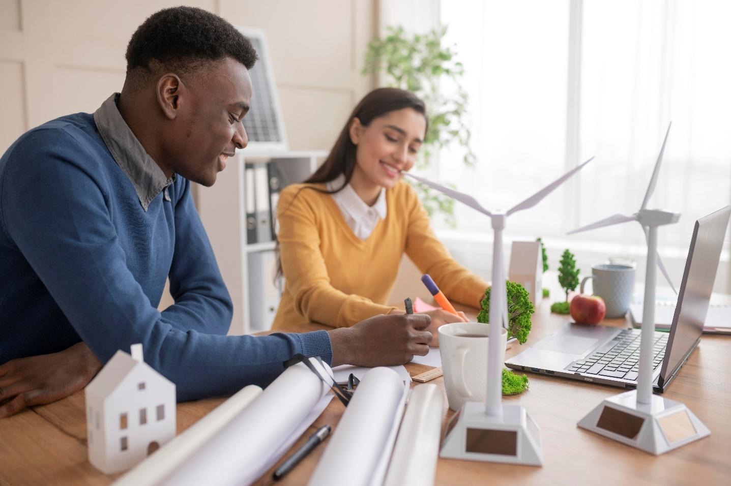 Un homme et une femme qui travaillent sur un ordinateur près de maquettes de maisons et d'éolienne