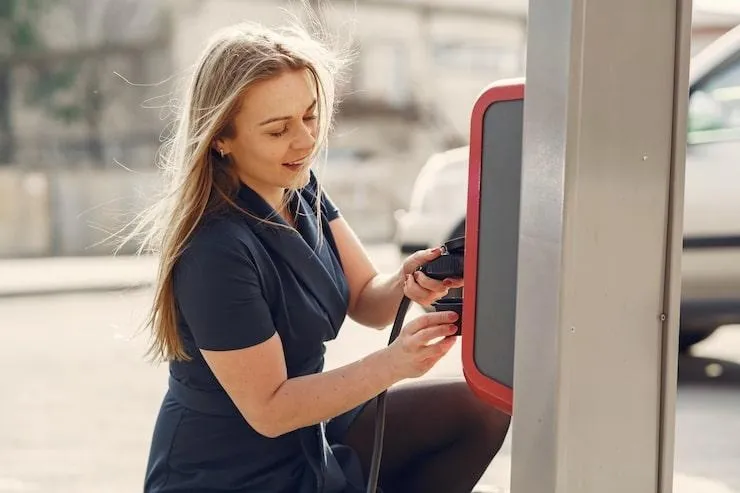 Une femme entrain de brancher une prise sur une borne de recharge électrique