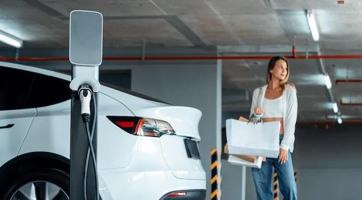 Une femme debout près d'une voiture et d'une borne de recharge électrique dans un parking