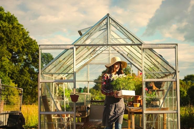 Une femme qui tient un pot de fleur devant une serre en verre et en métal