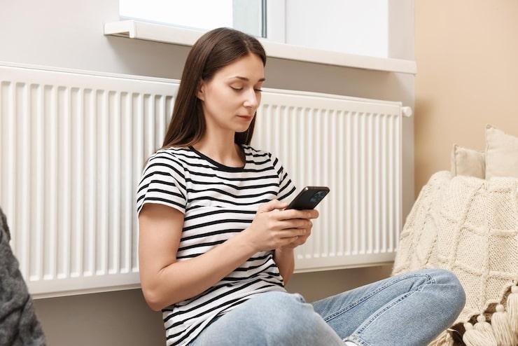 Une femme sur son smartphone assis contre un radiateur install contre un mur