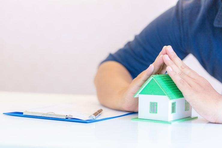 Un homme qui protège une maquette de maison posée sur la table avec ses mains