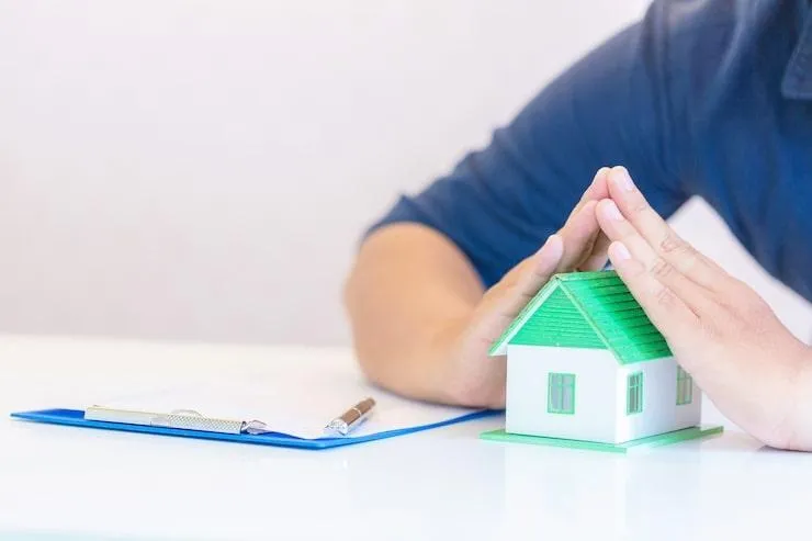 Un homme qui protège une maquette de maison posée sur la table avec ses mains