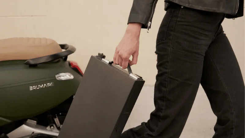 Un homme qui marche dans une rue urbaine en tenant dans sa main les batteries de son scooter électrique de marque Brumaire