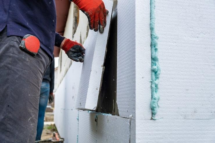 Un chauffagiste qui installe des blocs de polystyrène sur un mur extérieur