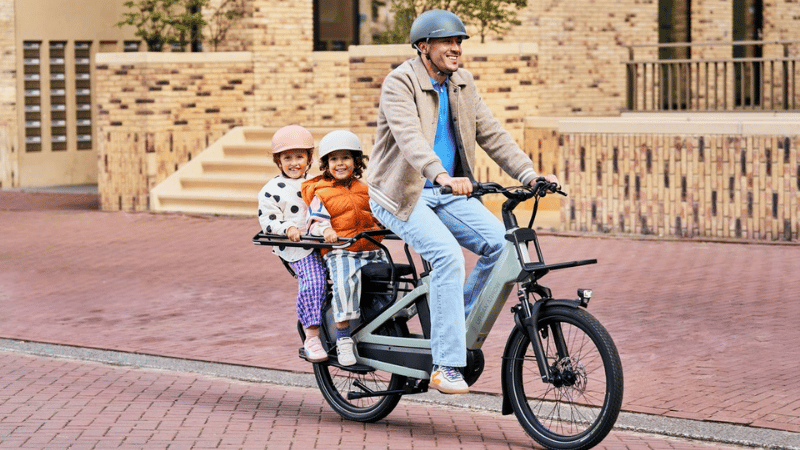 Homme qui est sur un vélo longtail avec ses deux enfants à l’arrière.