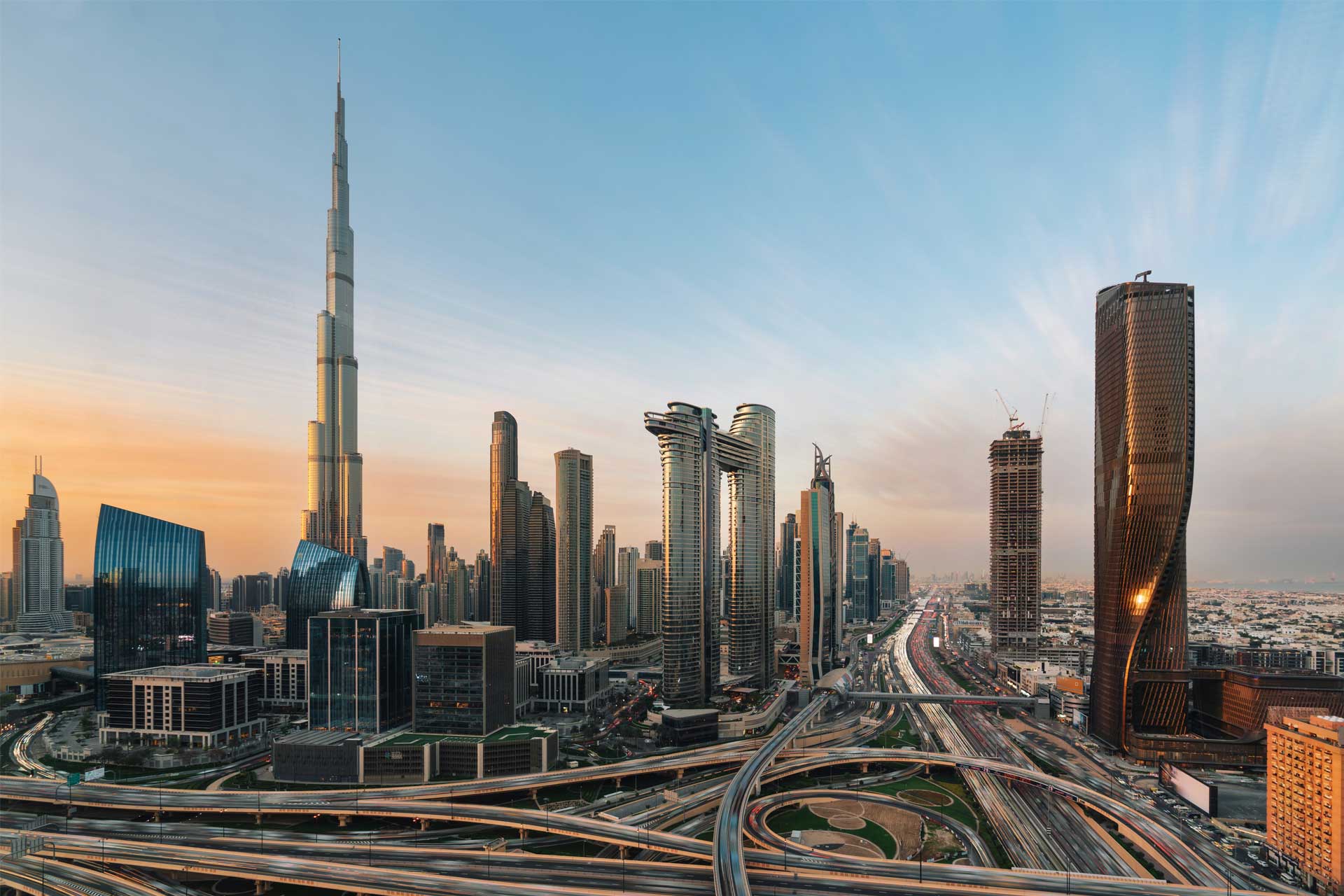 Sunset view of Dubai skyline featuring Burj Khalifa, modern skyscrapers, and busy multi-level highways.