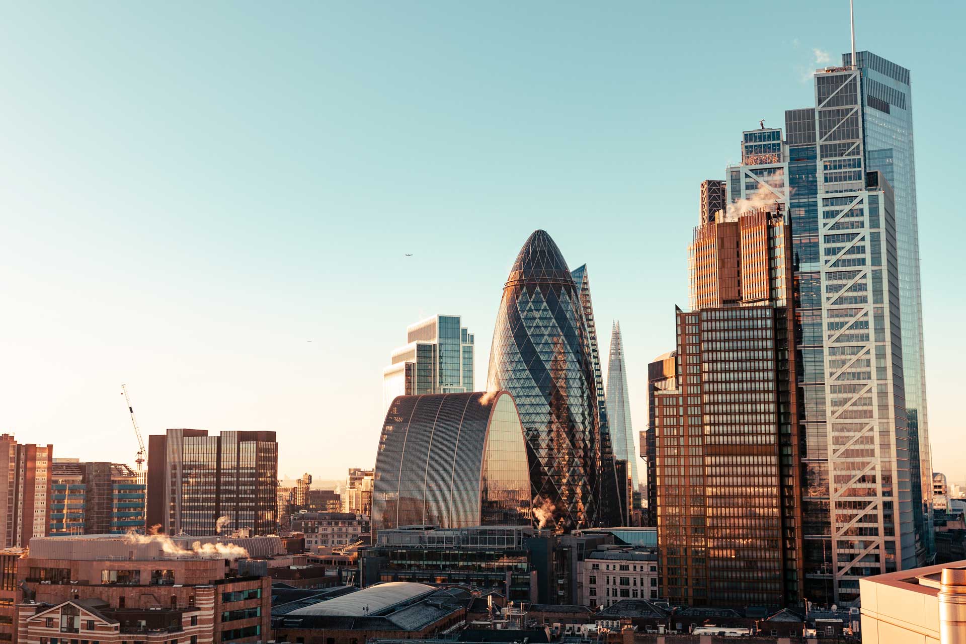 London cityscape with iconic modern skyscrapers including the Gherkin and the Shard under clear sky at sunset.