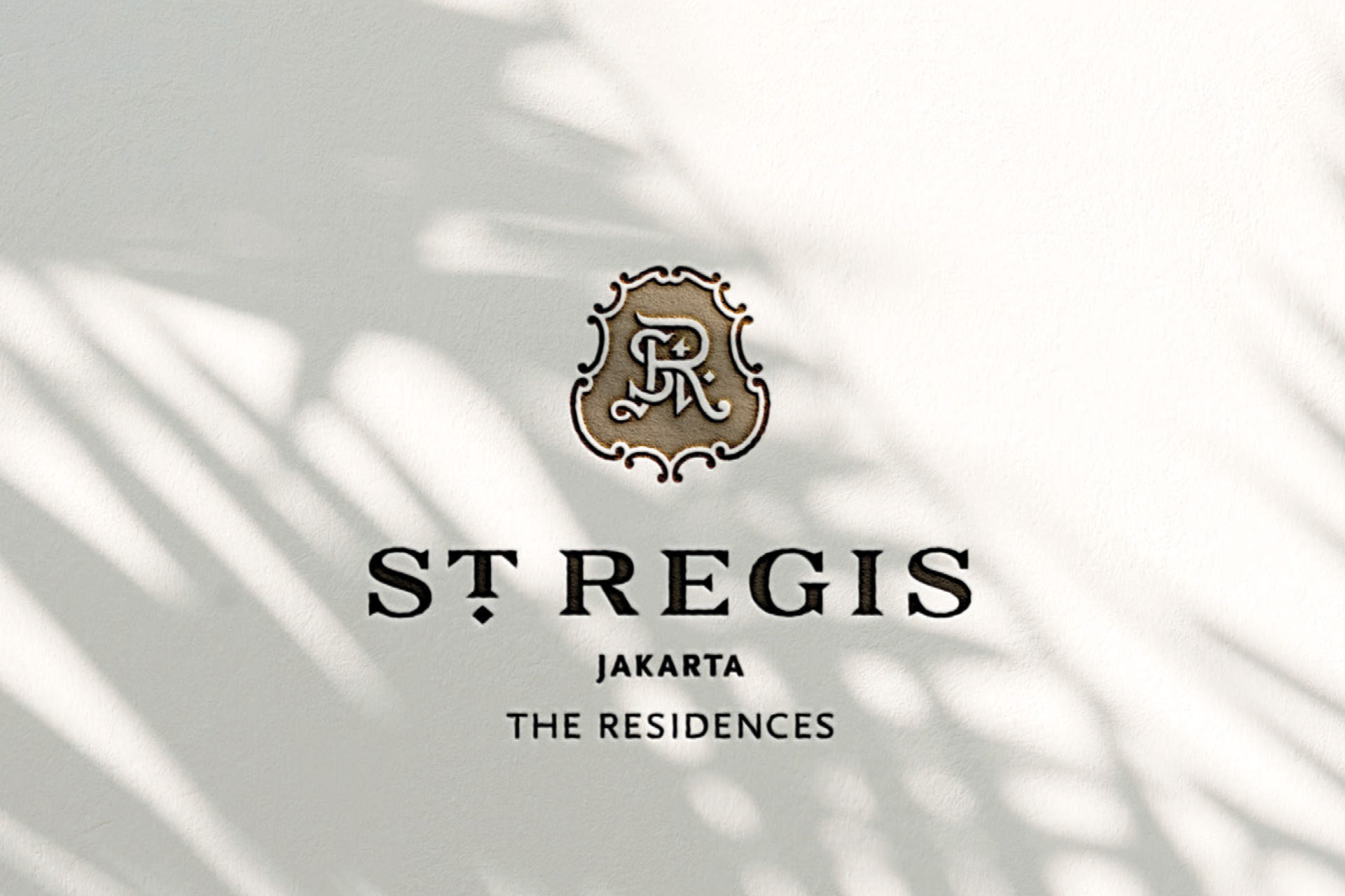 St Regis Jakarta The Residences logo with decorative emblem on a light textured wall with palm shadows.