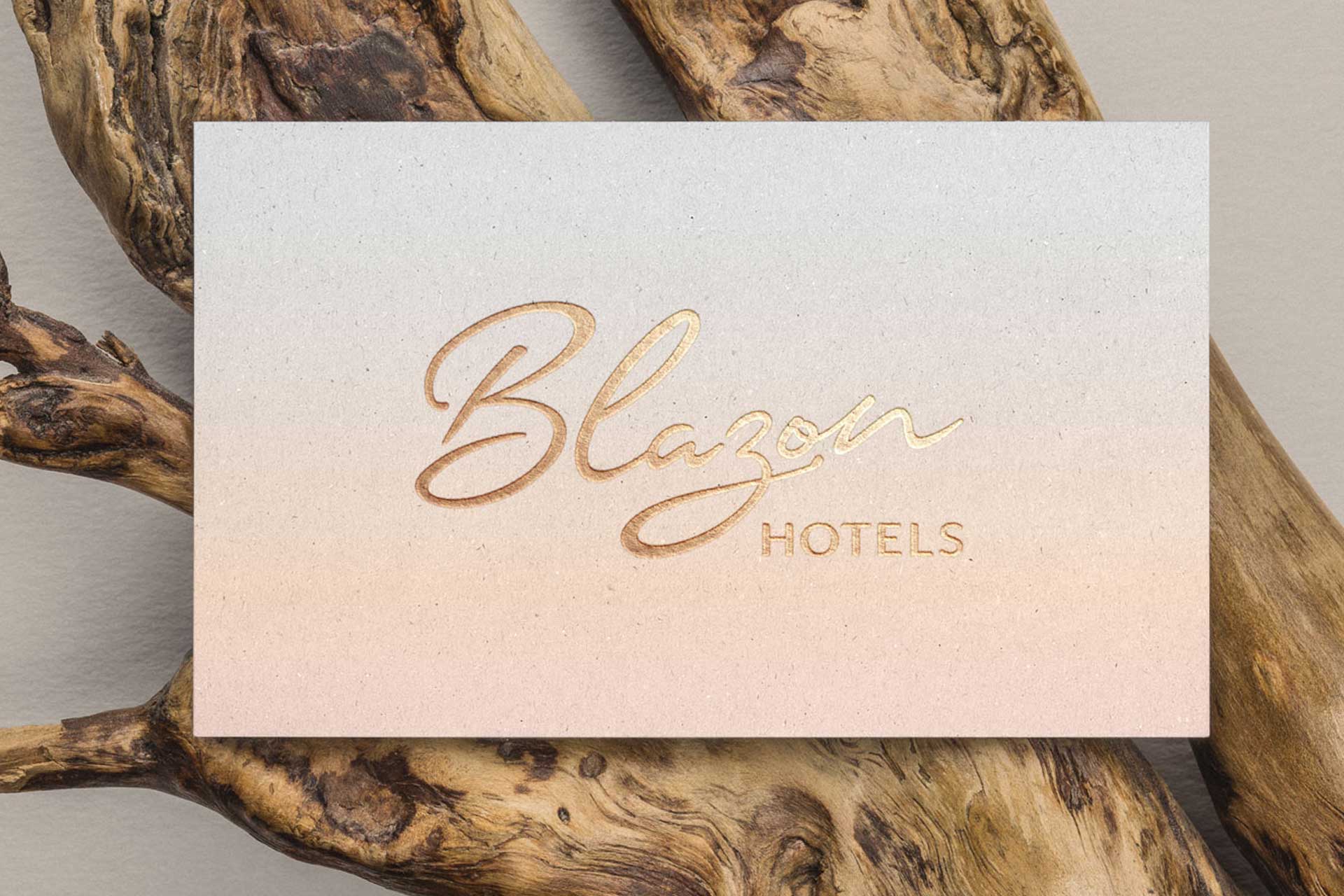 Business card with a gradient background featuring 'Blazon Hotels' in elegant gold lettering placed on rustic wooden branches.