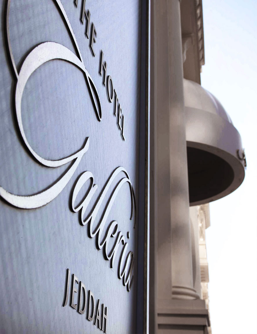 Close-up of a metallic sign that reads 'The Hotel Galleria Jeddah' mounted on a building exterior with architectural details.