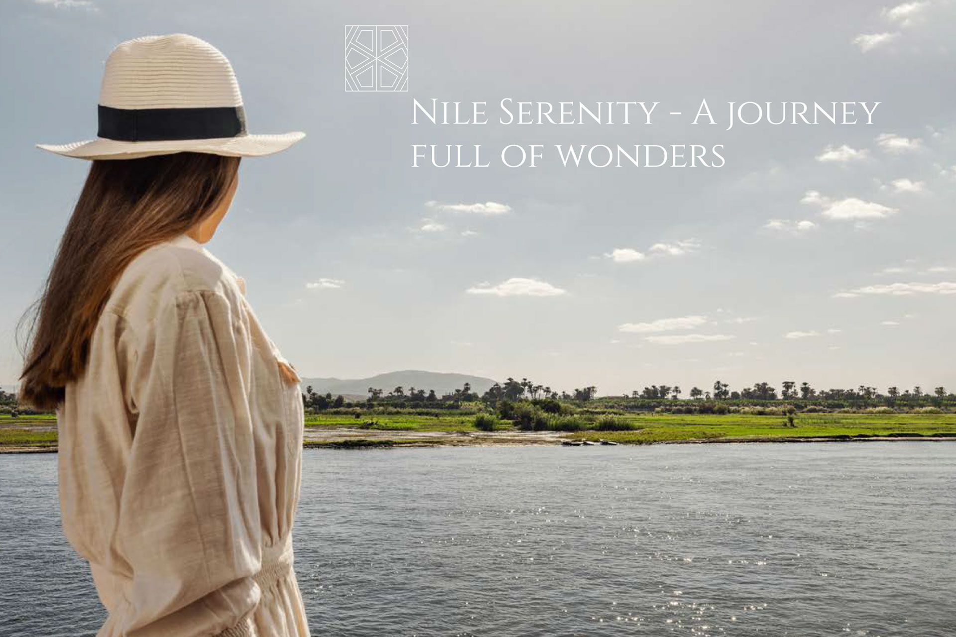 Woman wearing a hat and beige dress looking out at a calm river with green fields and palm trees under a partly cloudy sky.