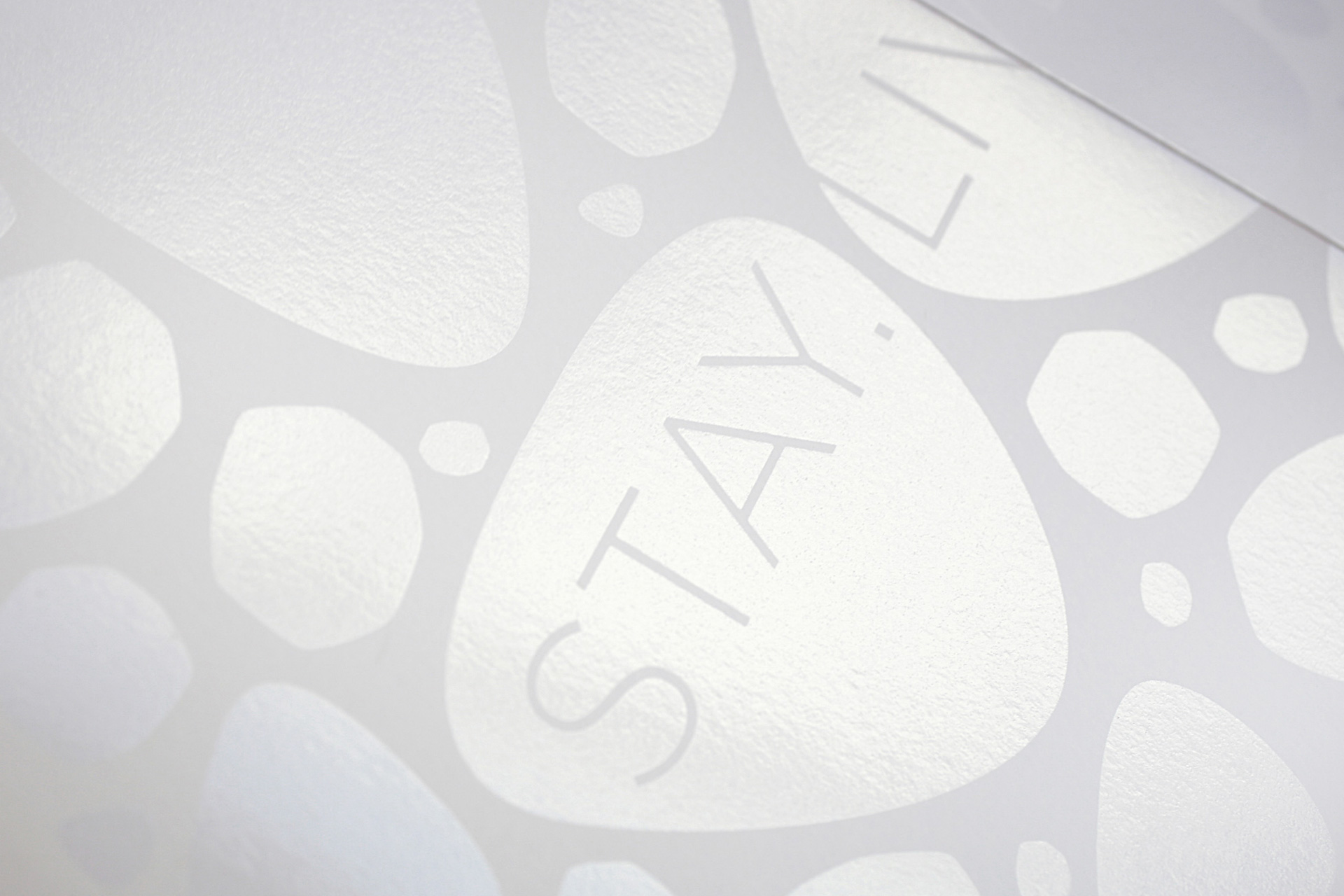 Close-up of a textured surface with abstract pebble shapes and the word 'STAY' embossed on one pebble.