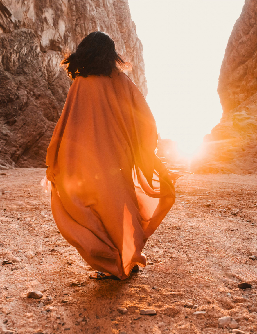 Woman with curly hair standing and looking at the pyramids of Giza at sunset.