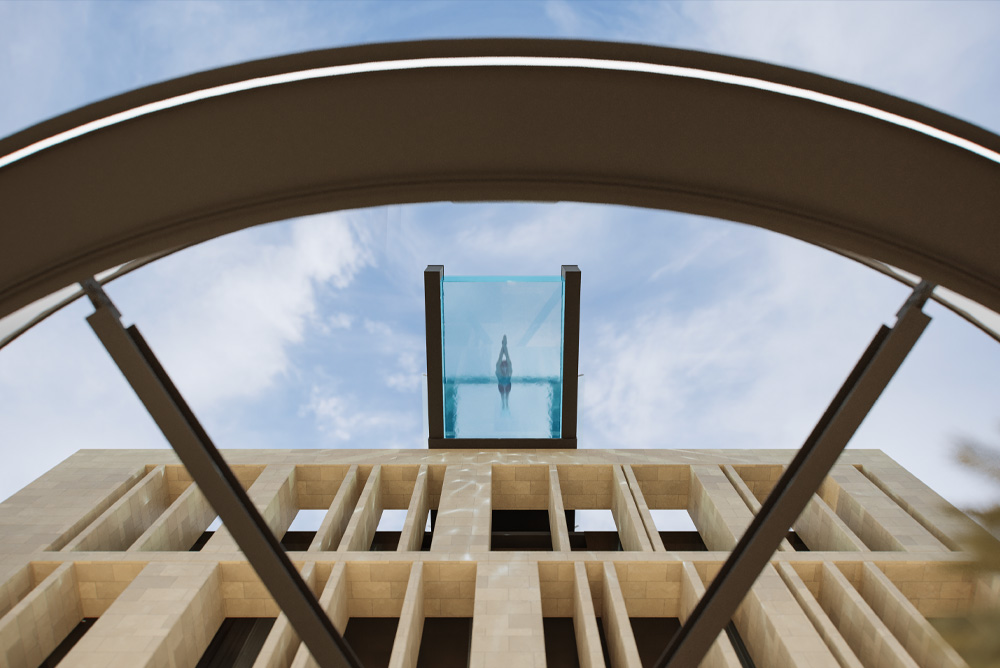 Person diving off a clear glass pool extending from a modern building against a blue sky.