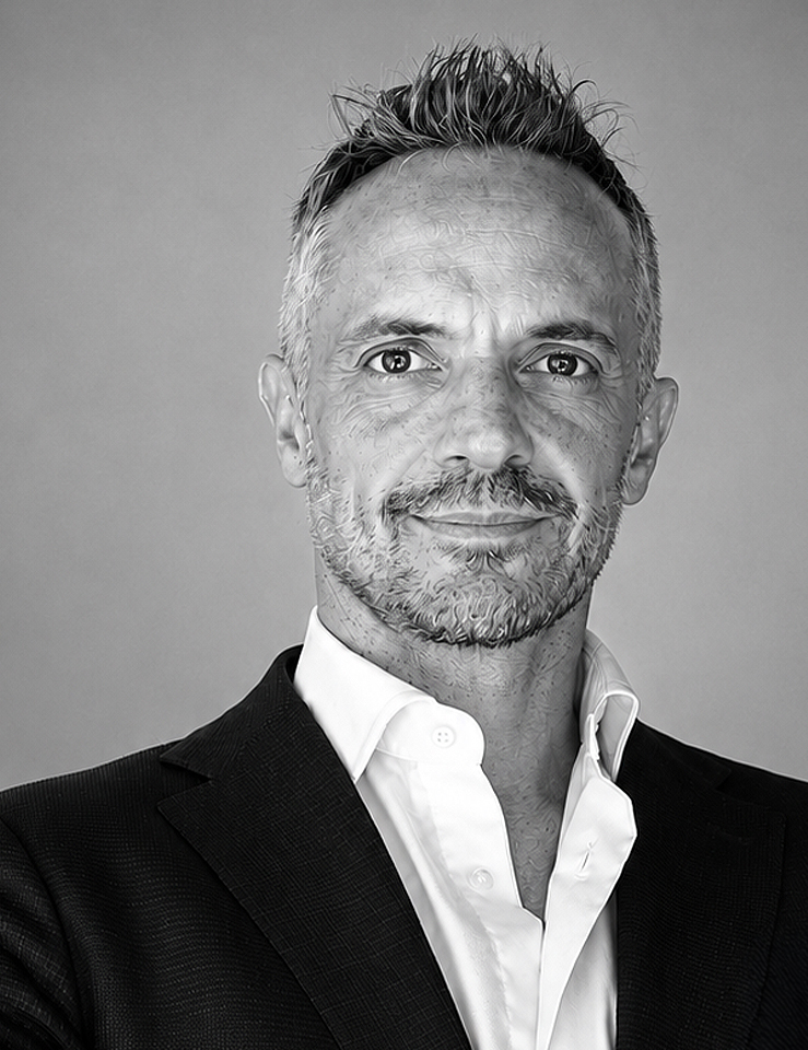 Black and white portrait of a man wearing a suit with an open-collar white shirt, neutral background.