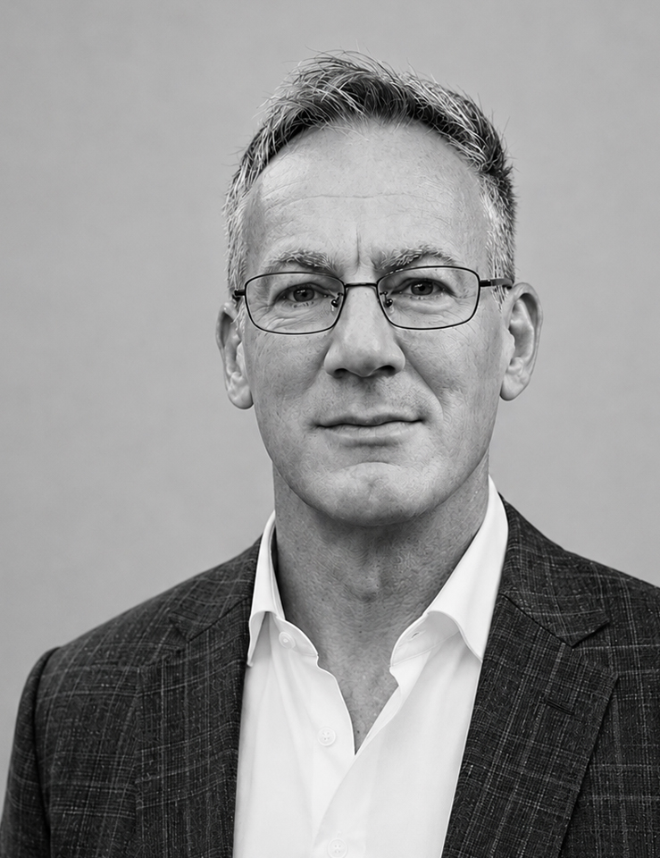 Black and white portrait of a middle-aged man wearing glasses, a white shirt, and a checkered blazer.