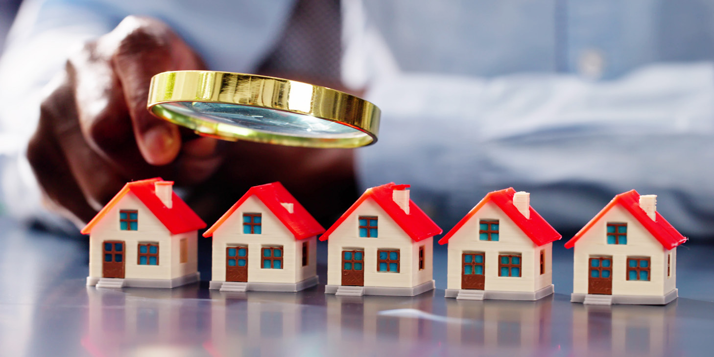 Close-up of a person examining miniature model houses with a magnifying glass, symbolizing real estate evaluation and community reserve studies.