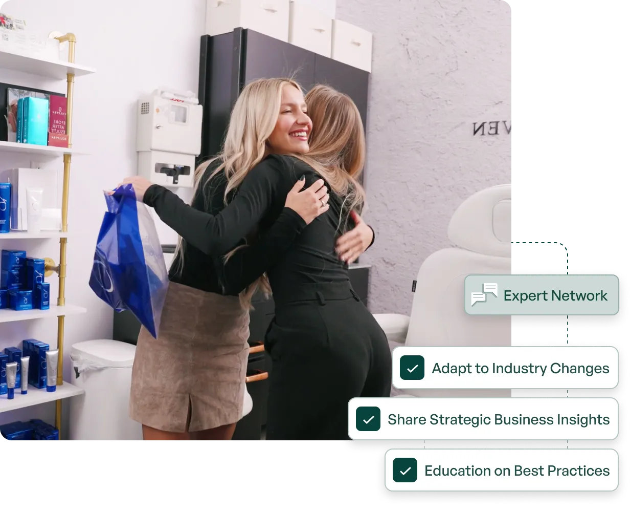 Two women hugging happily in a retail or office space, one holding a blue shopping bag.