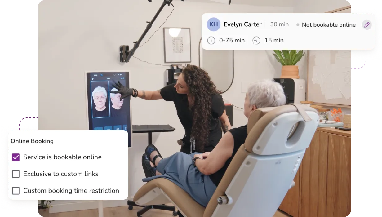 A professional shows facial images on a vertical screen to an elderly woman seated in a reclining chair in a modern office.